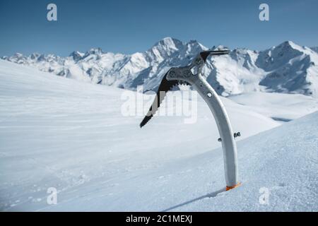 Gros plan d'une hache glacée dans la neige avec des montagnes enneigées en arrière-plan Banque D'Images