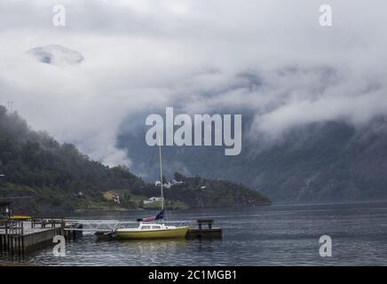 Petit bateau sur un lac calme brumeux avec des montagnes en arrière-plan Banque D'Images
