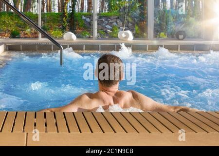 Bel homme dans le bain à remous spa en hôtel de luxe avec de grandes baies vitrées avec vue sur la nature. Banque D'Images