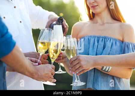 Des amis heureux versant du champagne mousseux dans des verres à l'extérieur sur une plage Banque D'Images