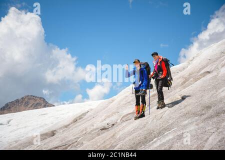 Deux touristes, un homme et une femme avec des sacs à dos et des chats à leurs pieds, se tiennent sur la glace, sur le fond des montagnes Banque D'Images