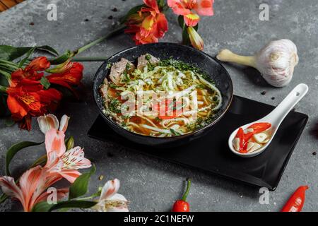 Cuisine asiatique, soupe de bœuf dans une assiette noire sur fond sombre. Soupe au bouillon de bœuf épicé, filet de bœuf, nouilles udon, pâte de Chili Banque D'Images