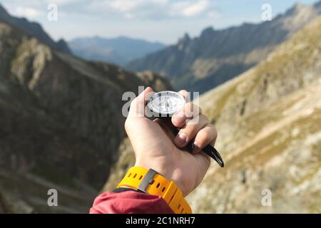 La main d'un homme tient un compas magnétique de poche pour la navigation sur fond de pente rocheuse et de montagne. Le concept de Banque D'Images