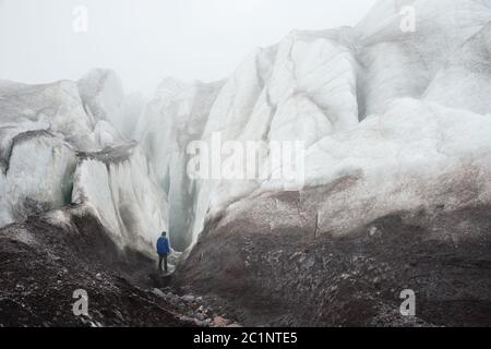 Un grimpeur libre avec une hache de glace à la main se tient au pied du Grand Glacier à côté d'une fissure épique dans le brouillard de la mounta Banque D'Images