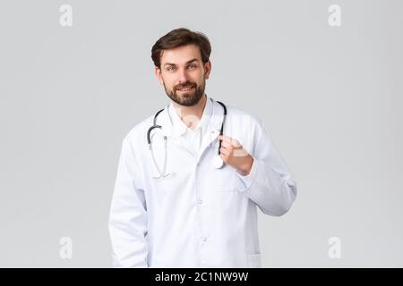 Hôpital, personnel de santé, concept de traitement Covid-19. Beau barbu médecin dans des exfoliations blanches avec stéthoscope, sourire au patient, à l'écoute Banque D'Images