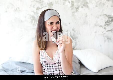 Jeune femme souriante et gaie dans une chemise blanche mangeant une barre de chocolat Banque D'Images