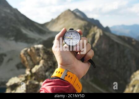 La main d'un homme tient un compas magnétique de poche pour la navigation sur fond de pente rocheuse et de montagne. Le concept de Banque D'Images