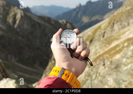 La main d'un homme tient un compas magnétique de poche pour la navigation sur fond de pente rocheuse et de montagne. Le concept de Banque D'Images