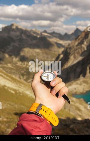 La main d'un homme tient un compas magnétique de poche pour la navigation sur fond de pente rocheuse et de montagne. Le concept de Banque D'Images