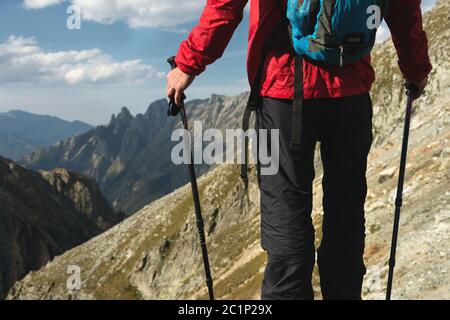 Le corps de l'homme avec un sac à dos et des bâtons de randonnée se dresse sur le dessus d'un rocher contre l'arrière-plan de la vallée rocheuse haut dans le mont Banque D'Images