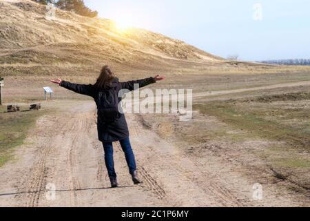 Stock Photo de portrait femme en manteau noir bras levés sur la route vide vers le coucher du soleil l'horizontale Banque D'Images