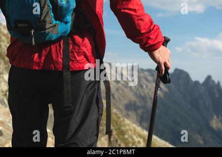 Gros plan corps de l'homme avec un sac à dos et des bâtons de randonnée se dresse sur le dessus d'un rocher contre le fond de la vallée rocheuse haut dans le Banque D'Images