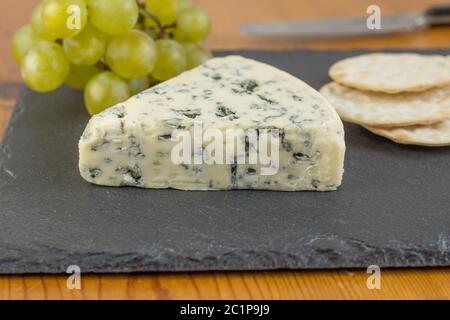 Fromage bleu ardoise sur board close up avec des raisins verts et les craquelins de flou artistique en arrière-plan Banque D'Images