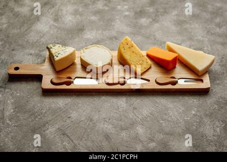 Assortiment de différents types de fromages servi sur planche de bois avec la fourchette et couteaux