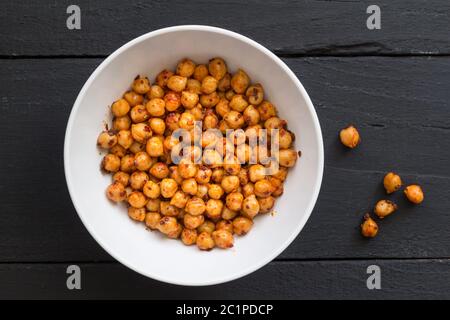 Pois chiches à l'huile d'olive et aux flocons de piment - pois chiches épicés dans un bol blanc sur fond rustique noir Banque D'Images