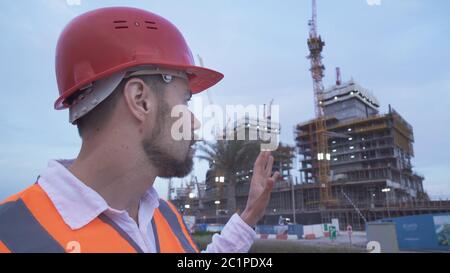 L'homme à un casque, architecte, ingénieur, gestionnaire parle de l'avancement des travaux de construction en soirée Banque D'Images