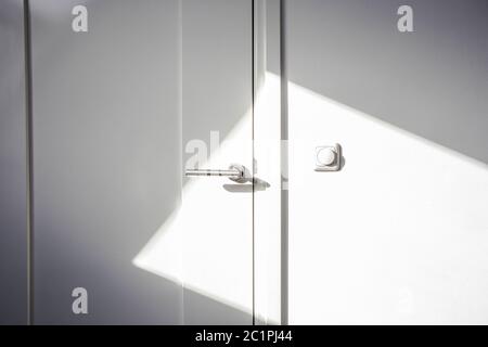 Close-up porte blanche avec la lumière du soleil. Chrome de porte ,l'interrupteur d'éclairage sur le mur vide et propre de conception moderne Banque D'Images