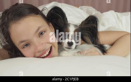 Happy teen girl kisses et joue avec chien Papillon au lit Banque D'Images