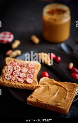 Toasts de pain avec beurre de cacahuète fait maison servi avec des tranches de canneberges fraîches Banque D'Images