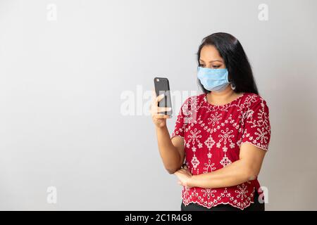 Une femme indienne tient son téléphone tout en portant un masque à la maison Banque D'Images