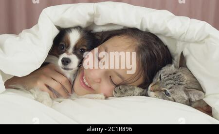 Happy teen girl communique avec chien Papillon et Thai cat in bed Banque D'Images