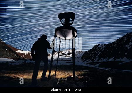 Silhouette d'homme près de l'ancien appareil météorologique avec la lumière de tête est de regarder les montagnes de nuit ciel avec des pistes étoiles Banque D'Images