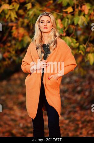 Adorable petite fille blonde posing in outfit chaleureux et cosy de l'automne nature fond flou. L'heure du coucher du soleil à pied femme. Tenues décontractées confortable pour la fin de l'automne. L'ambiance chaleureuse et confortable. Création pour agréable fin de semaine. Banque D'Images