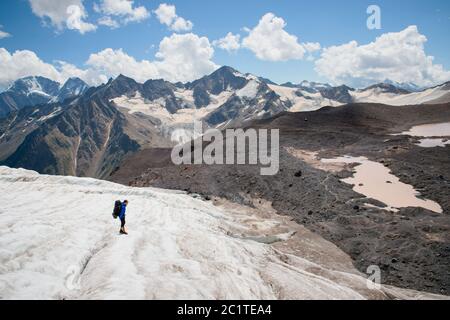 Un alpiniste avec un sac à dos marche dans des crampons le long d'un glacier poussiéreux avec des trottoirs dans les mains entre les fissures dans le Banque D'Images