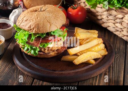 Délicieux burger au poulet, bacon, tomate, fromage et laitue servis avec frites Banque D'Images