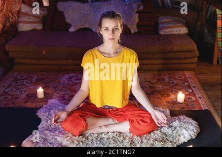 Portrait d'une jeune fille en vêtements brillants pratiquant la méditation dans une salle de confection entourée de bougies. Direction du nouveau-âge et Banque D'Images