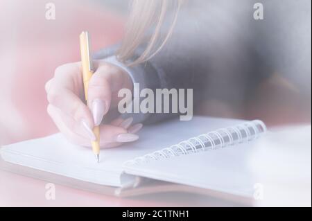 Gros plan de la main d'une étudiante dans un café derrière le verre avec une réflexion qui écrit quelque chose avec un stylo à bille dans un Banque D'Images