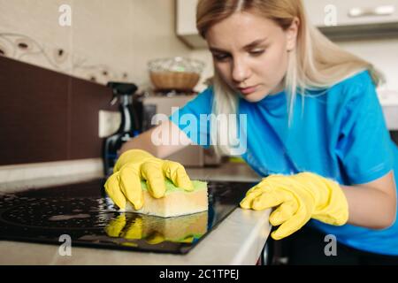 Femme, portant dans gant de protection avec chiffon de nettoyage, cuisinière électrique à la maison. Banque D'Images