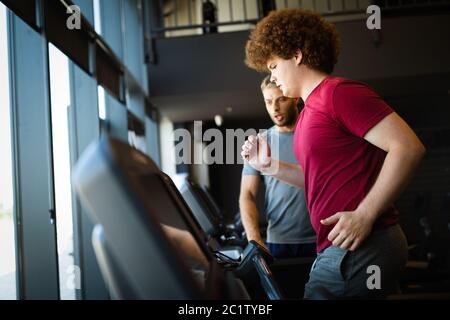 Surpoids jeune homme faisant de l'exercice de salle de gym avec entraîneur personnel Banque D'Images