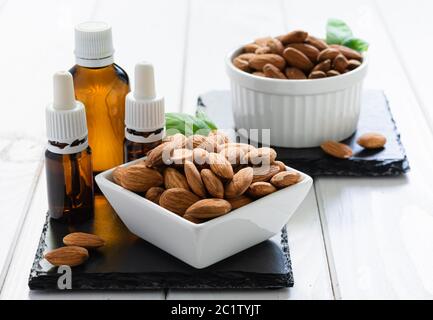 amandes en plaque blanche et bouteilles de verre avec huile sur un plateau noir sur une table en bois Banque D'Images