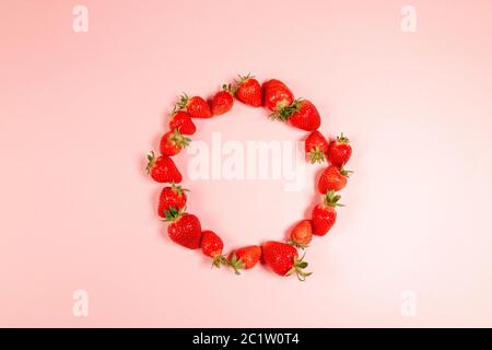 Cadre fait de fraises coupées en deux dans un cercle sur fond rose Banque D'Images