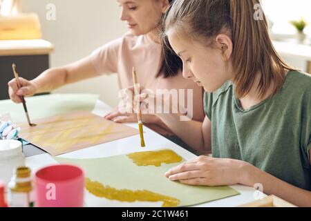 Elle a concentré sa fille adolescente à table et à l'aide de peintures tout en faisant des photos avec sa mère Banque D'Images