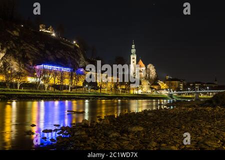 L'extérieur de l'église Pfarrkirche Mülln (paroisse catholique romaine) de Salzbourg la nuit depuis la rive de la rivière. D'autres bâtiments sont visibles. Il y a des Banque D'Images