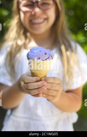 Jolie petite fille avec expression drôle tenant le cône de glace dehors sur fond de nature lumineux Banque D'Images