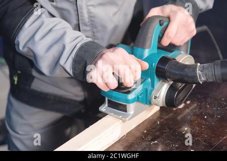 Gros plan de la main d'un menuisier travaillant avec un avion électrique avec aspiration de sciure. Nivellement et ponçage des barres en bois Banque D'Images