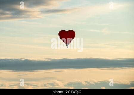 Ballon coloré en forme de coeur de grand air chaud volant contre le ciel nuageux Banque D'Images