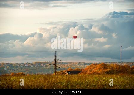 Ballon coloré en forme de coeur d'air chaud volant contre le ciel nuageux dans la campagne, le soir d'automne Banque D'Images