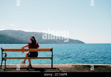 Femme méconnue vue de derrière assise sur un banc au bord de la mer. Montagnes et mer sans fin au loin. Rive de la ville de Starigrad Croatie Banque D'Images