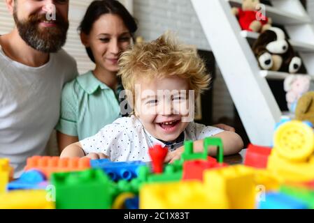 Couple dans le salon avec bébé souriant. Les parents regardent leur fils jouer avec des blocs colorés Banque D'Images