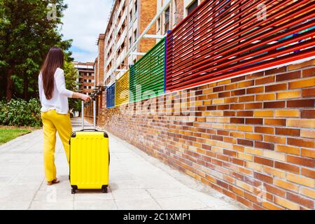 femme à son dos avec une valise jaune qui attend dans la rue Banque D'Images