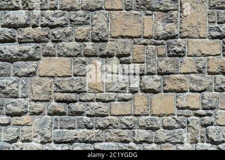 Vieux mur de pierre brun gris de pierres naturelles rugueuses, proéminentes au soleil Banque D'Images