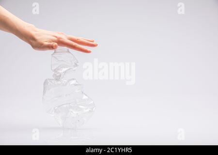 Gros plan de la main d'un peuple blanc écrasant une bouteille en plastique froissés devant un fond blanc Banque D'Images