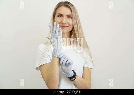 Jeune fille énergique belle met des gants. Joyeuse femme amicale attend le client et se prépare pour le travail. Spécialiste du salon de beauté. Banque D'Images