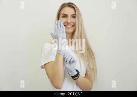 Jeune fille énergique belle met des gants. Joyeuse femme amicale attend le client et se prépare pour le travail. Spécialiste du salon de beauté. Banque D'Images