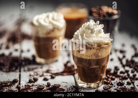 Café noir avec crème fouettée dans des tasses en verre et grains de café renversés Banque D'Images