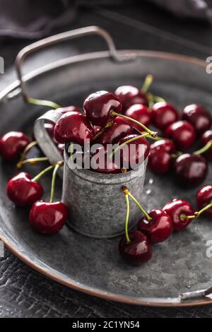 Plateau, surface et tasse vintage métallisé avec cerises juteuses rouges à l'intérieur de la tasse et dispersées autour du plateau Banque D'Images